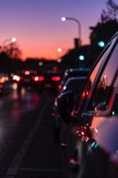 many cars are parked on the side of the road at night with street lights in the background