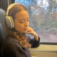 a young woman wearing headphones sitting on a train looking out the window while listening to music