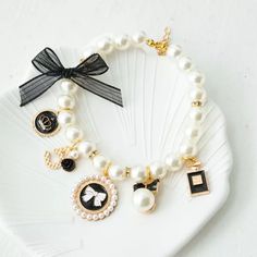 a white plate topped with a bracelet and charms on it's side next to a black bow