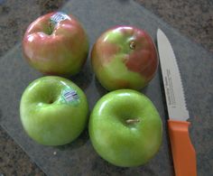 three green apples sitting on top of a cutting board next to a knife