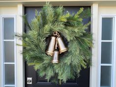 a wreath with two bells hanging from it's side on the front door,