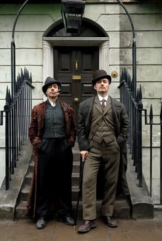 two men standing in front of a building with a black door and iron railings