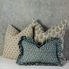 three decorative pillows sitting on top of a white table next to a gray and blue wall