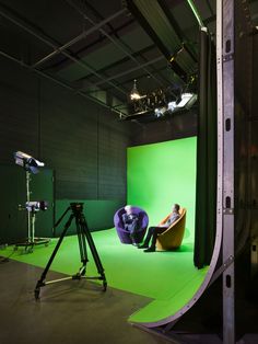 a person sitting in a chair on top of a green screen next to a tripod