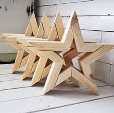 three wooden star shaped objects sitting on top of a white wood floor next to a brick wall