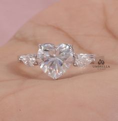 a heart shaped diamond ring on someone's hand