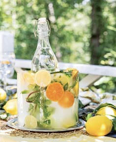 a glass bottle with lemons and oranges in it on top of a table