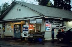 an old gas station with signs on the side of it and a car parked in front