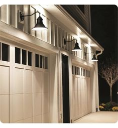 two lights are on the side of a white garage door at night with trees in the background