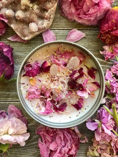 a bowl filled with lots of flowers on top of a wooden table covered in petals