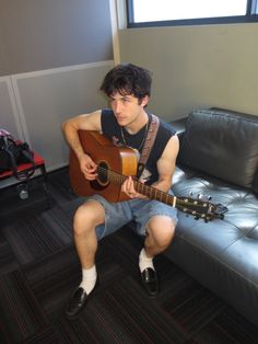 a man sitting on a couch playing an acoustic guitar