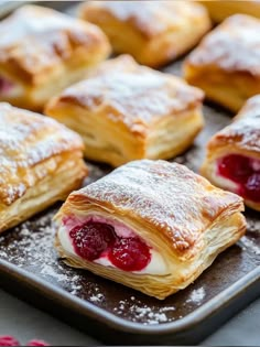 several pastries on a baking sheet with powdered sugar and raspberry filling