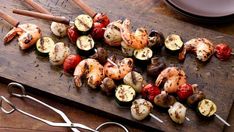 a wooden cutting board topped with skewered vegetables and shrimp on skewers