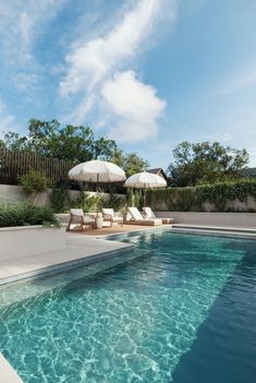 an empty swimming pool with lounge chairs and umbrellas next to it on a sunny day