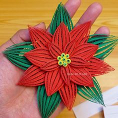 a hand holding an origami flower on top of a wooden table