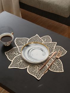 a black table topped with a white plate and two gold spoons next to a cup of coffee