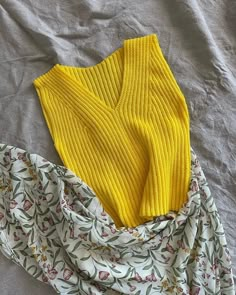 two yellow sweaters laying on top of a bed next to a white flowered blanket