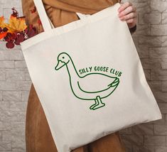 The Silly Goose Tote Bag is the perfect accessory for those who want to add a touch of humor to their everyday style. Made from durable canvas, this funny gag gift will not only put a smile on your face but also serve as a practical companion for carrying your essentials. With its spacious design and sturdy handles, it's the ideal choice for a lighthearted yet functional bag. Beach Tote Bags Diy, Decorated Tote Bags, Creative Tote Bag, Handpainted Tote, Handpainted Tote Bags, Bag Painting, Canvas Bag Design, Funny Tote Bags, Best Tote Bags