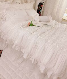 a white bed with ruffled bedspread and flowers on the end table next to it