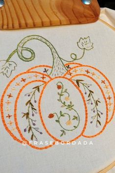 an embroidered pumpkin with leaves and vines is on a wooden cutting board next to a piece of wood