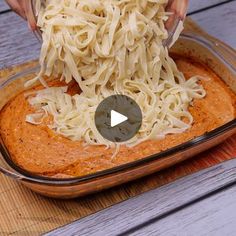 someone scooping noodles from a casserole dish into a glass pan on a wooden table