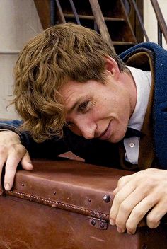 a man leaning on top of a brown suitcase with his hand on the back of it