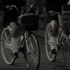 two people riding bikes down the street with baskets on their back's wheels, in black and white