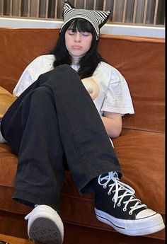 a woman sitting on top of a brown couch wearing black and white converse shoes with cat ears