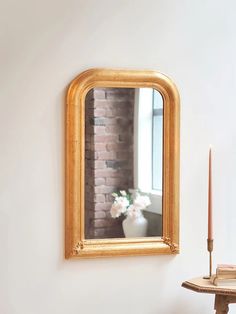 a mirror hanging on the wall next to a table with a candle and flowers in it