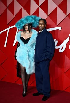 a man and woman standing next to each other in front of a red wall with the word trust written on it