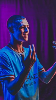 a man standing in front of a purple background holding his hands up to the side