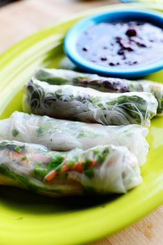 three spring rolls on a green plate with dipping sauce in the bowl next to them