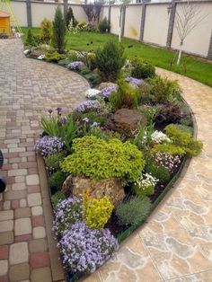 a garden with flowers and rocks on the side of a brick walkway in front of a house