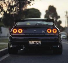 the rear end of a black car driving down a street with other cars behind it