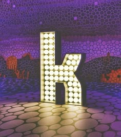 the letter k is lit up with lights in front of a purple and blue background