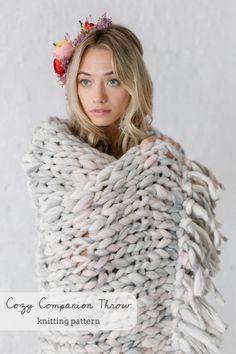 a woman is wrapped up in a large knitted blanket with flowers on her head