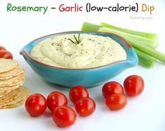 a blue bowl filled with dip surrounded by crackers and tomatoes next to celery