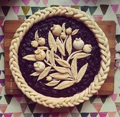 a pie that is sitting on top of a wooden cutting board with leaves and nuts