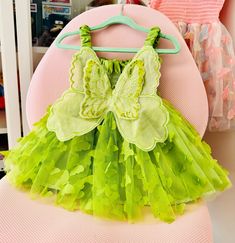 a green and yellow dress hanging on a hanger next to a pink chair in a child's room