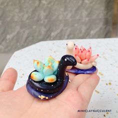 two small figurines sitting on top of each other in the palm of someone's hand