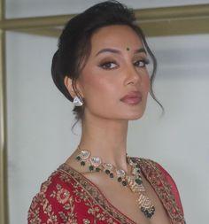 a woman in a red sari with jewelry on her neck and shoulders, looking off to the side