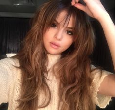 a woman with long brown hair wearing a white sweater and holding her hand on her head