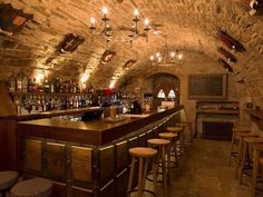 a bar with lots of stools and bottles hanging from the ceiling in an old stone building