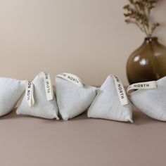 three small white pillows sitting on top of a table next to a vase with flowers