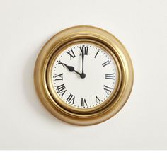 a gold clock with roman numerals on the face is shown against a white wall