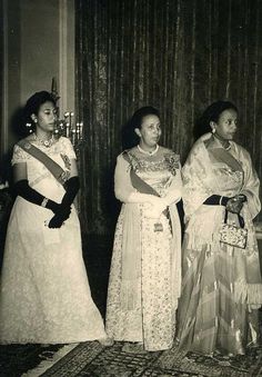 three women standing next to each other in formal dress and tiaras, all wearing sashes