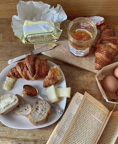 an open book and some bread on a table next to eggs, butter, cheese and other food items