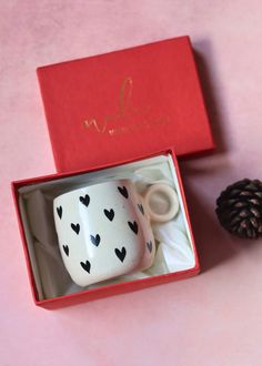 two coffee mugs in a red box with black hearts on them and a pine cone