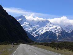 an empty road with snow capped mountains in the background