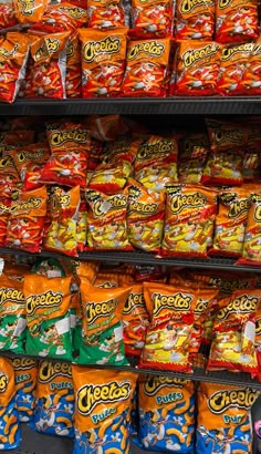 many bags of chips are on display in a store shelf with other snacks behind them